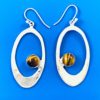 Round tiger eye stone with bands of brown and gold set in silver and surrounded by a large flat silver oval dangling from silver ear wires